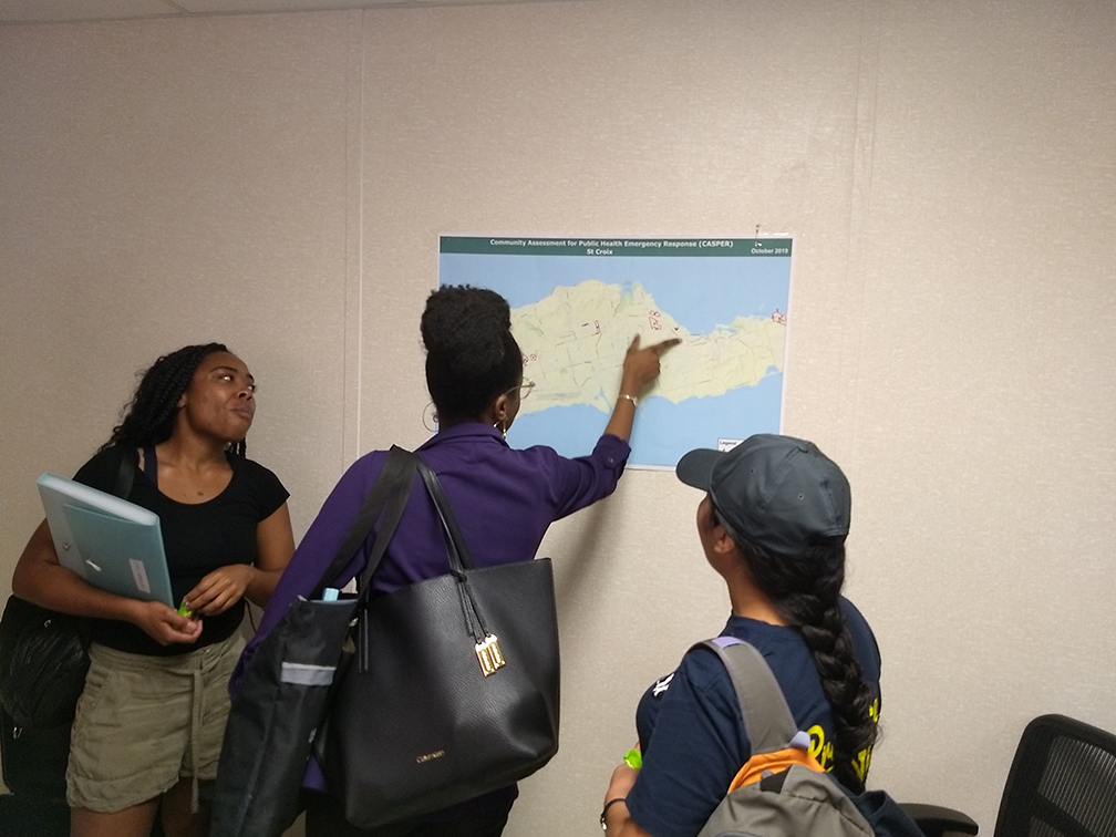Kayla Hunter and Quetzabel Benavides with community partner at Department of Health examining map of St. Croix survey clusters.